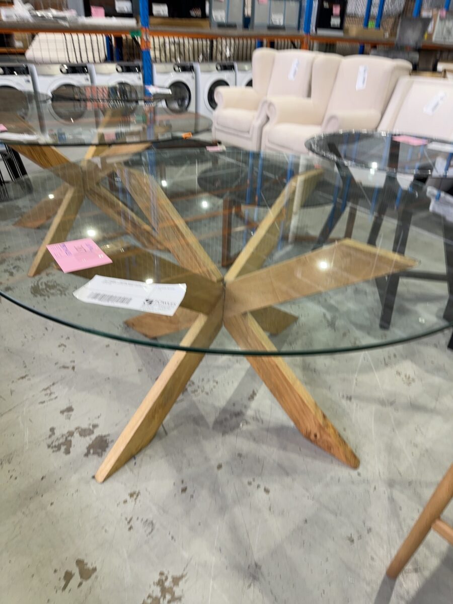 EX STAGING - 1500MM ROUND GLASS TABLE, WITH TIMBER CROSS LEG BASE, CHIPPED EDGE ON GLASS