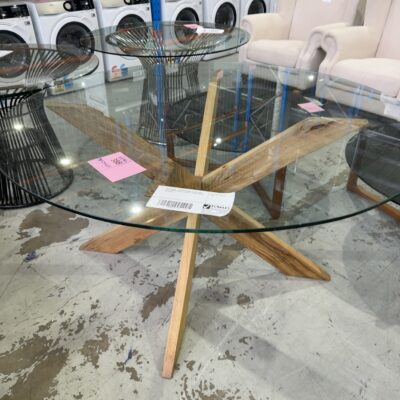 EX STAGING - 1500MM ROUND GLASS TABLE, WITH TIMBER CROSS LEG BASE, CHIPPED EDGE ON GLASS