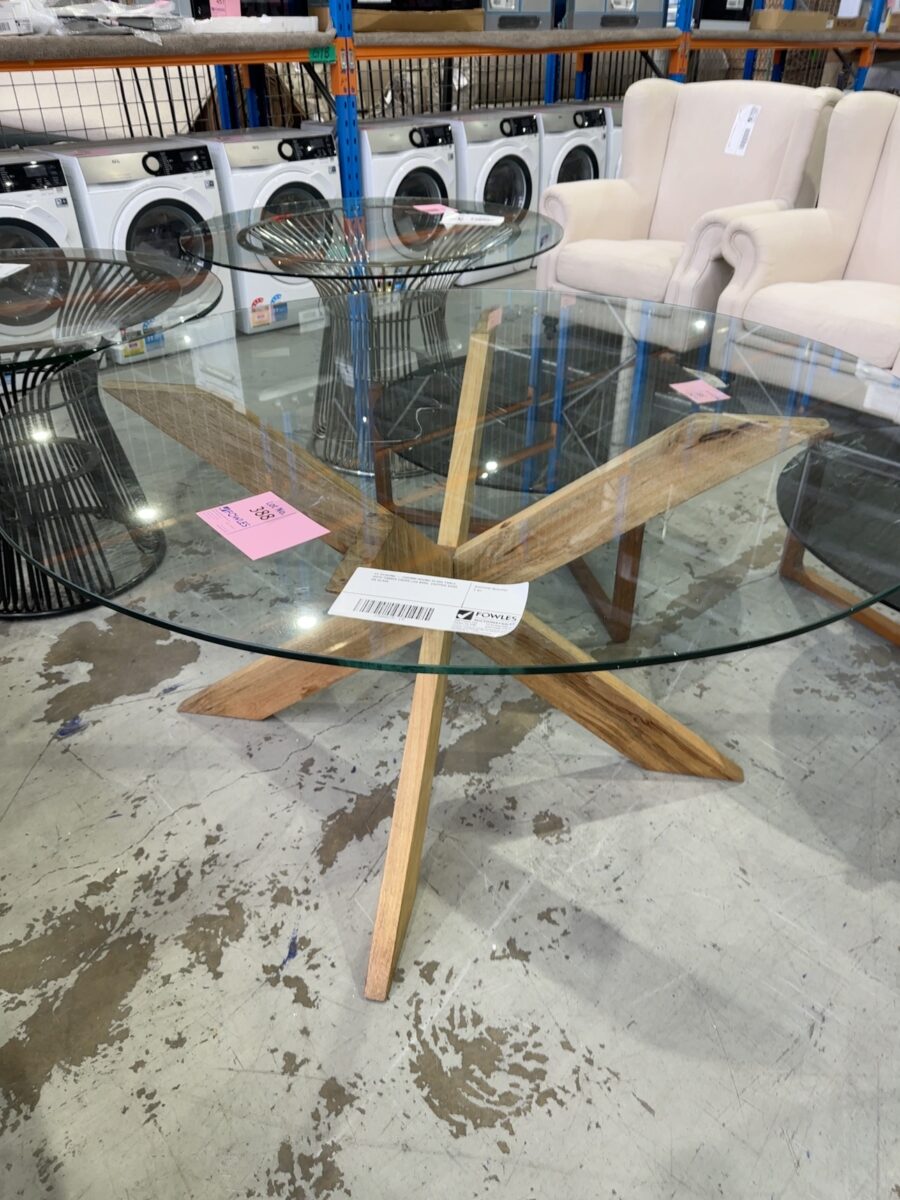 EX STAGING - 1500MM ROUND GLASS TABLE, WITH TIMBER CROSS LEG BASE, CHIPPED EDGE ON GLASS